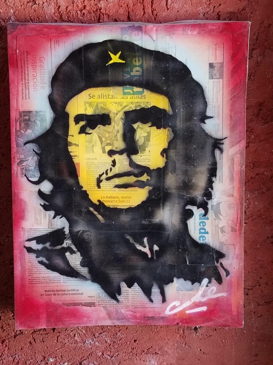 A portrait of Che Guevara layered over Cuban newspaper pages on a red wall